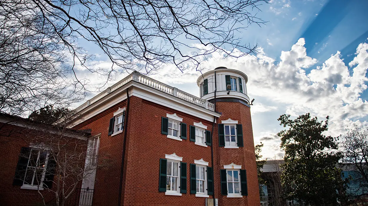 Exterior of antebellum red brick building with green shuttered windows and an observatory.