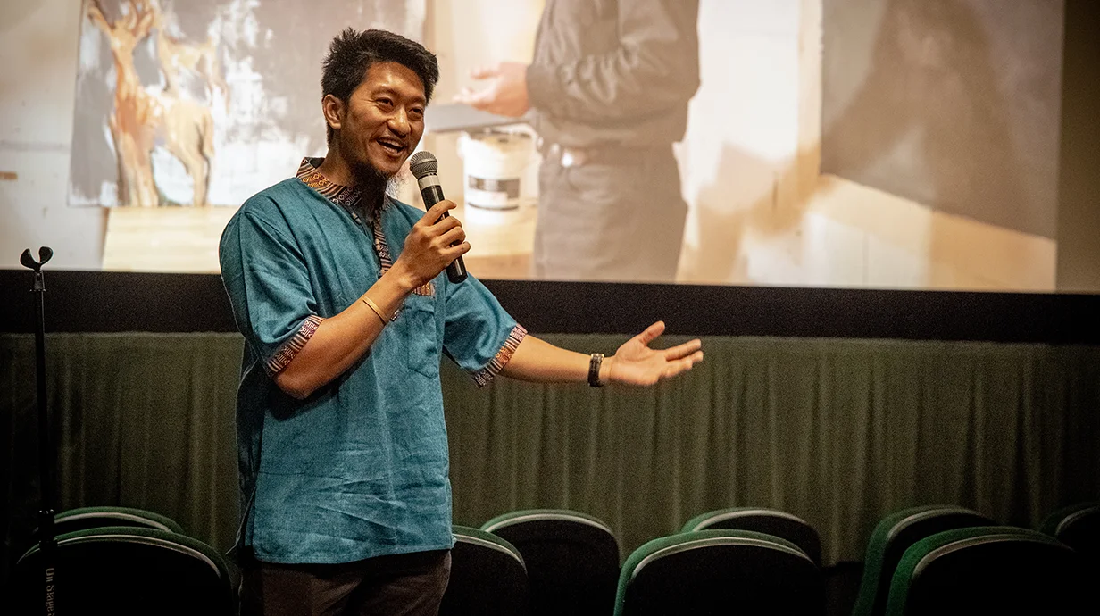 man standing in front of screen holding a microphone in a theater