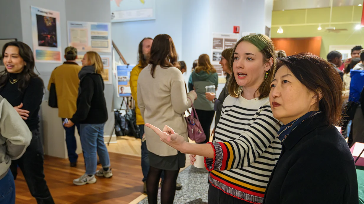 people standing around; two people in foreground are looking and pointing to something out of frame