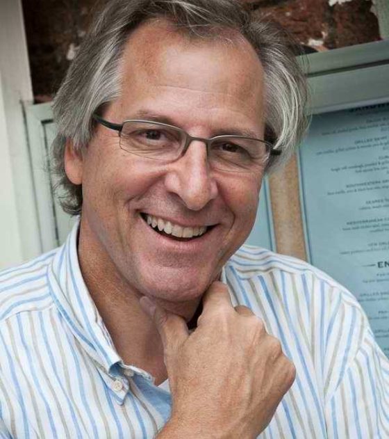 Portrait of smiling Tom Howorth, head tilted and hand at chin