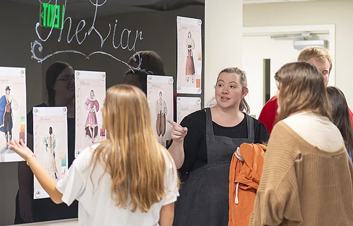 professor pointing to the wall, speaking to small group of students all standing 