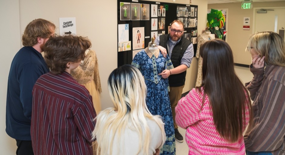 staff and students gathered around dress model and pin-up board of costumes in a hallway