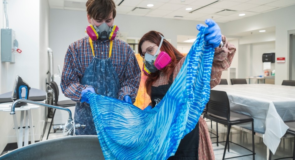 faculty and student pulling blue cloth out of dye vat