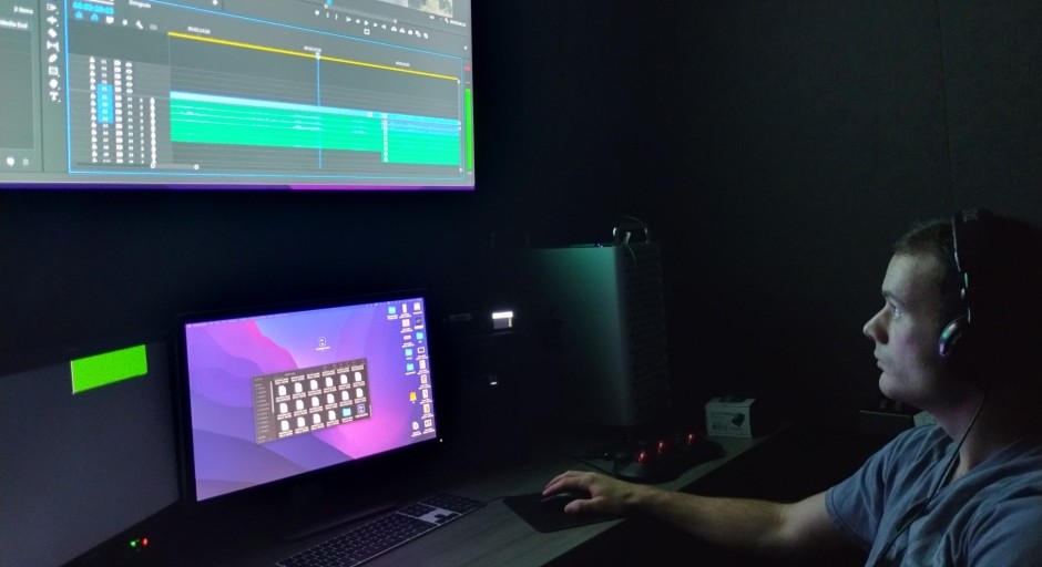 dark room with a student working at a computer screen and large TV screen