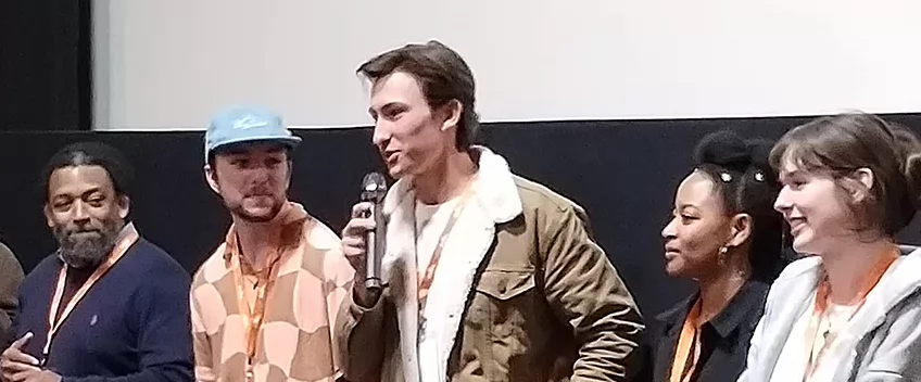 group of people standing in front of a movie screen. One person holds a microphone.