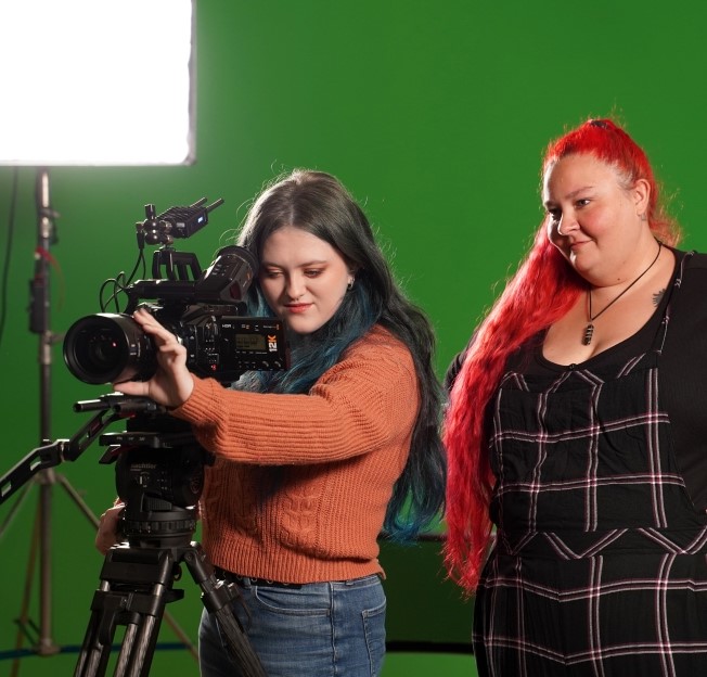 student standing behind a film camera while professor stands behind her