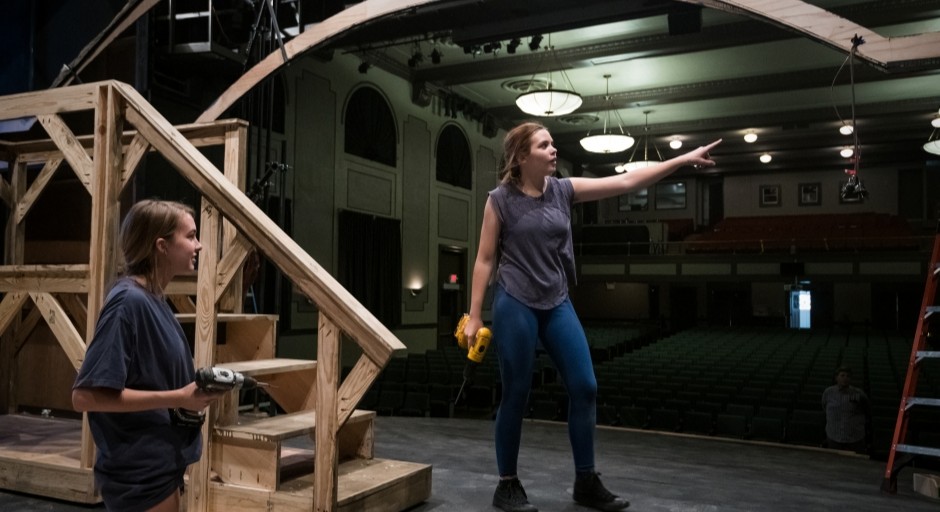 image of students holding tools and standing on stage while they build the theatre set