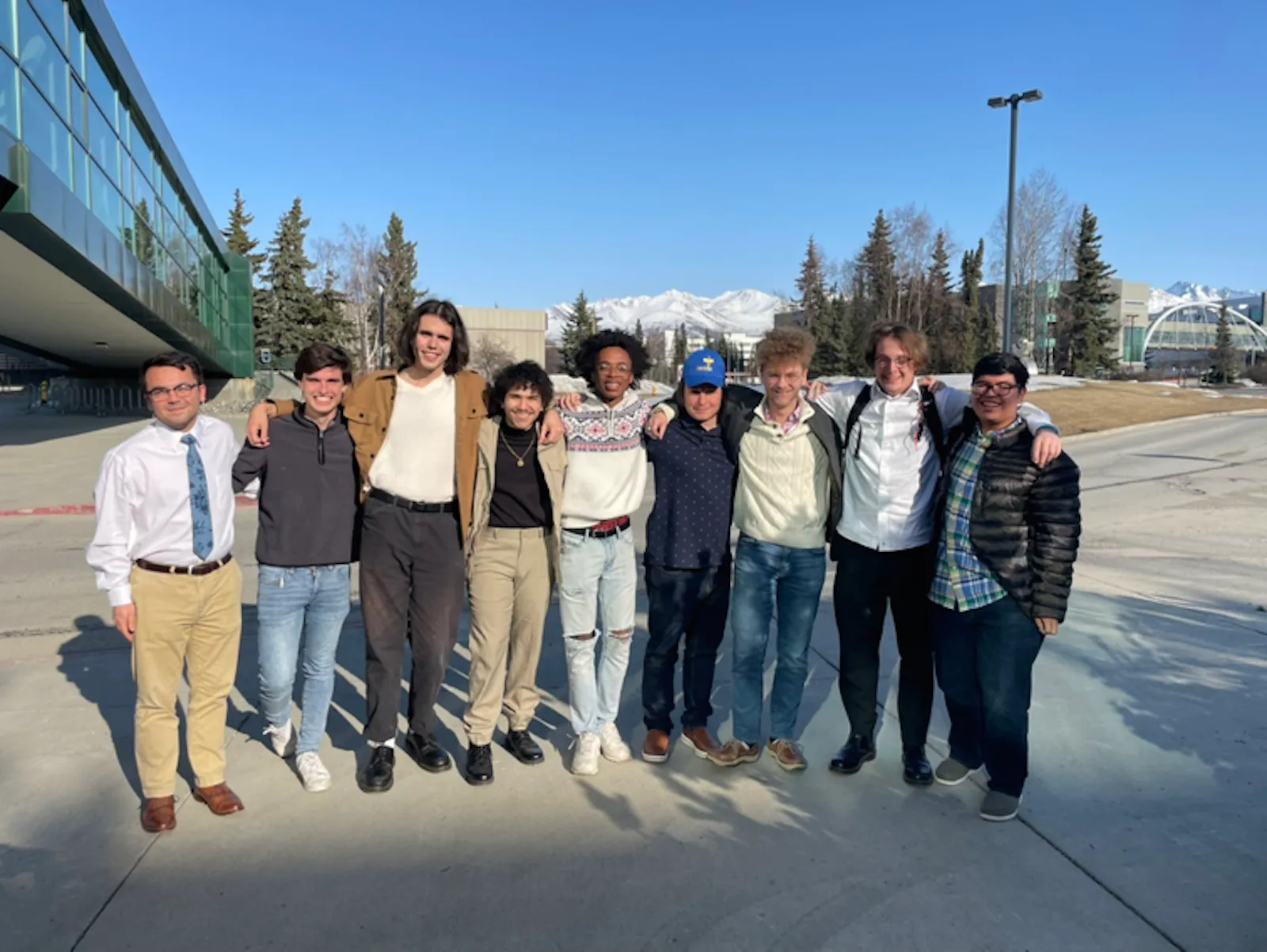 Large group of students standing outdoors on a sunny day; building and snow capped mountains in background