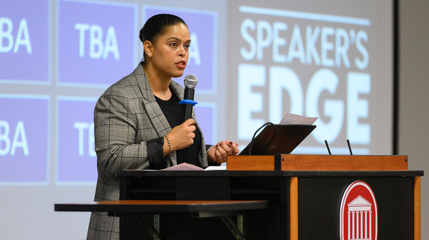 woman standing on stage holding a microphone behind a podium