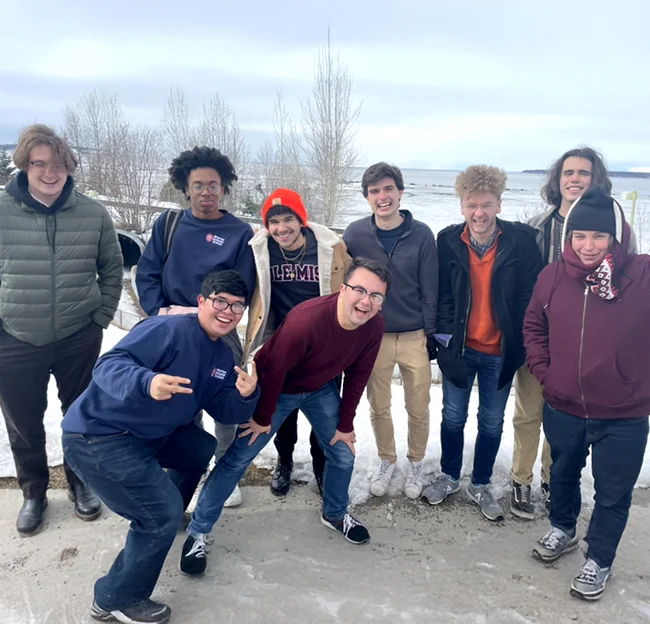Group of smiling students looking at the camera, wearing coats standing on a beach