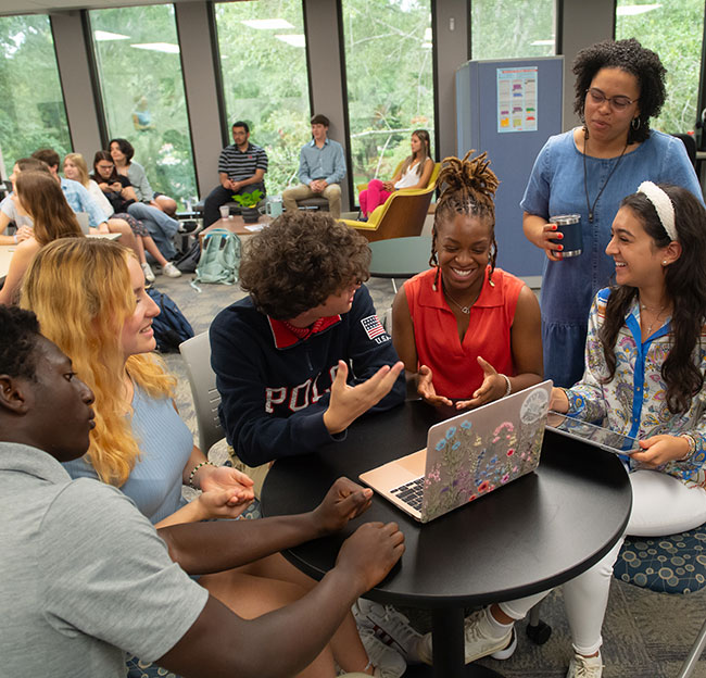 students sitting around a laptop and teacher in class