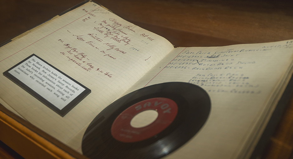 A display case holds a 45-rpm vinyl record sitting on an opened business ledger.