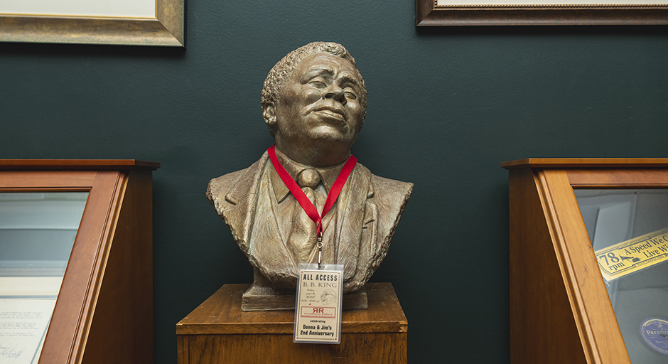 A sculpted bust of a man singing sits between two display cases.