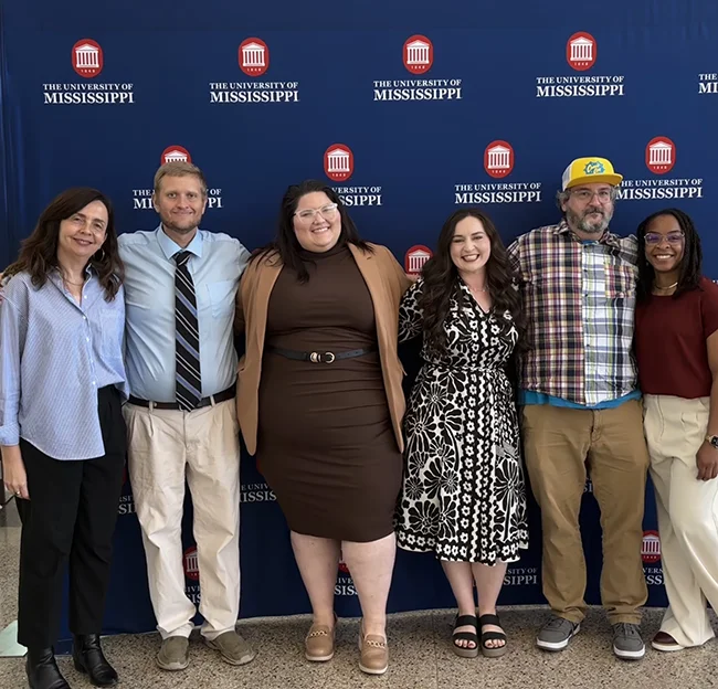 a group of people standing in front of a backdrop with the University of Mississippi on it