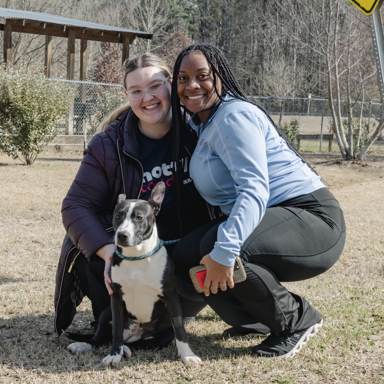 Two students pose with a dog while volunteering with an animal shelter
