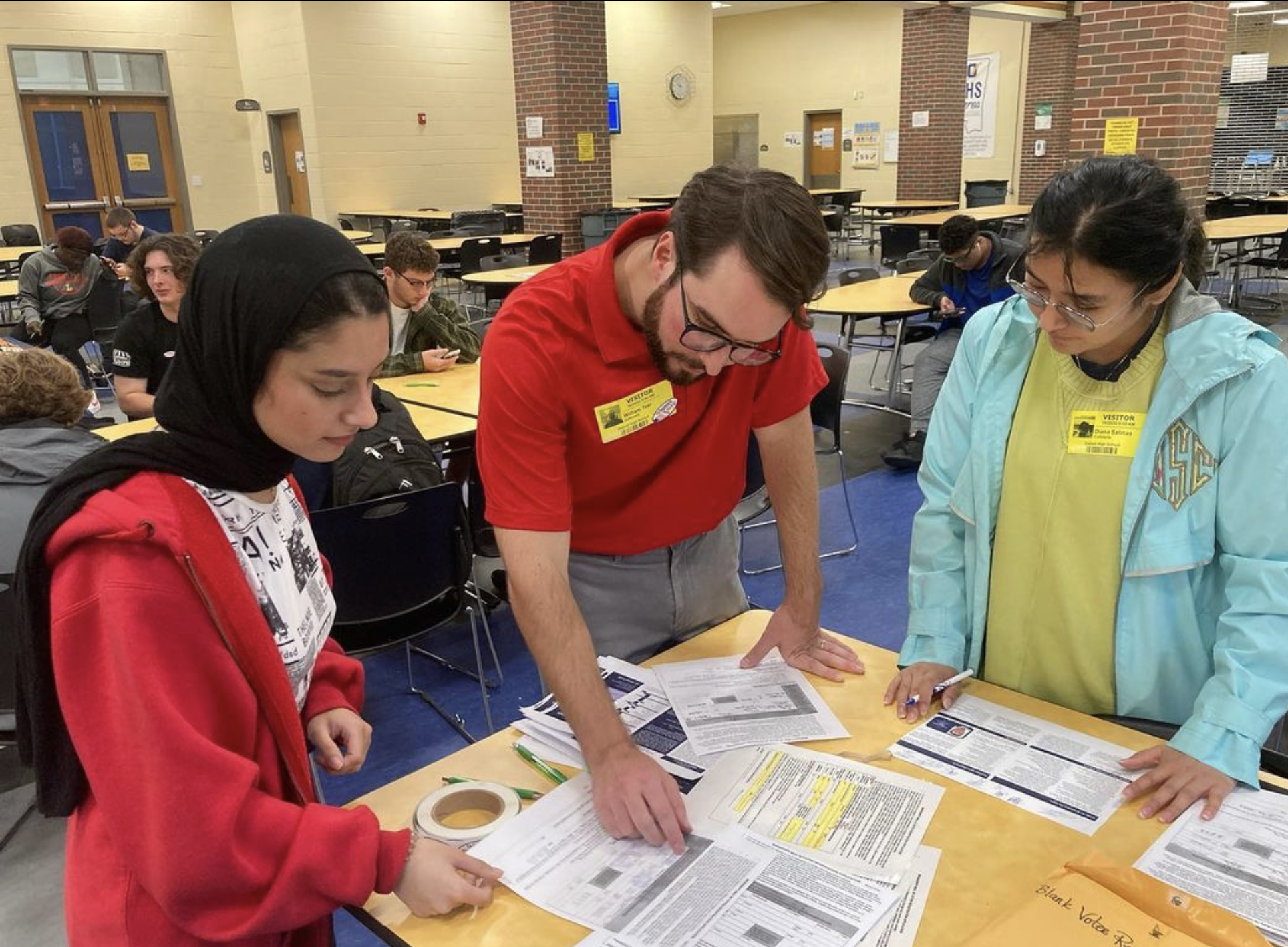 three people standing at a table looking at voter registration forms on the table