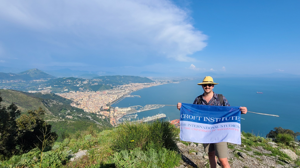 Croft student holding Croft flag on cliff top abroad