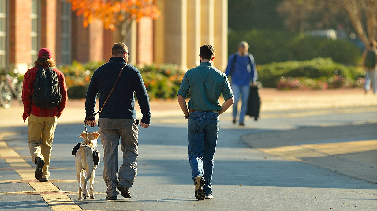 Two men walk down Business Row, one has a Service Animal leashed to his left side.