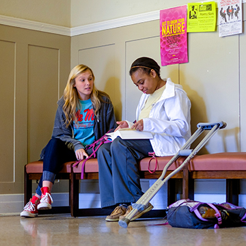 Two students study together on a bench. One has crutches sitting next to her.