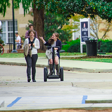 Two students commute to class while smiling, one on a assistive device.