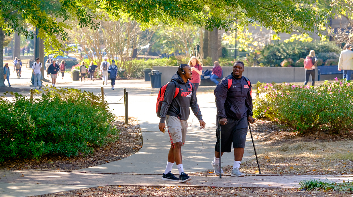 Two students smile and talk as they walk to class, one using an assisted walking device