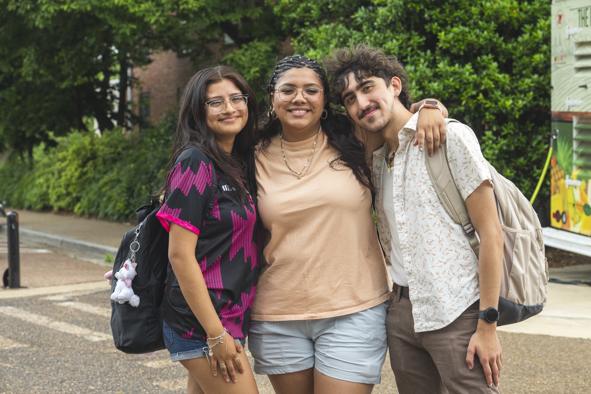 Three students embrace and smile on business row of the Ole Miss campus
