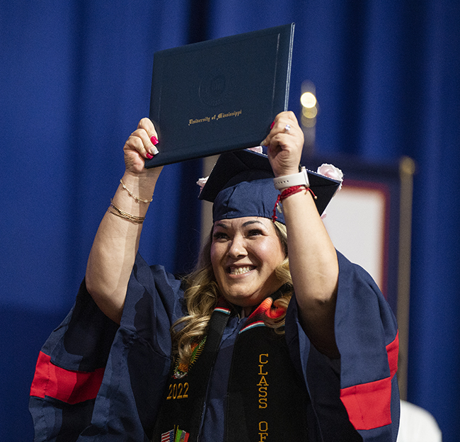 A student holds up her diploma proudly on stage at commencement