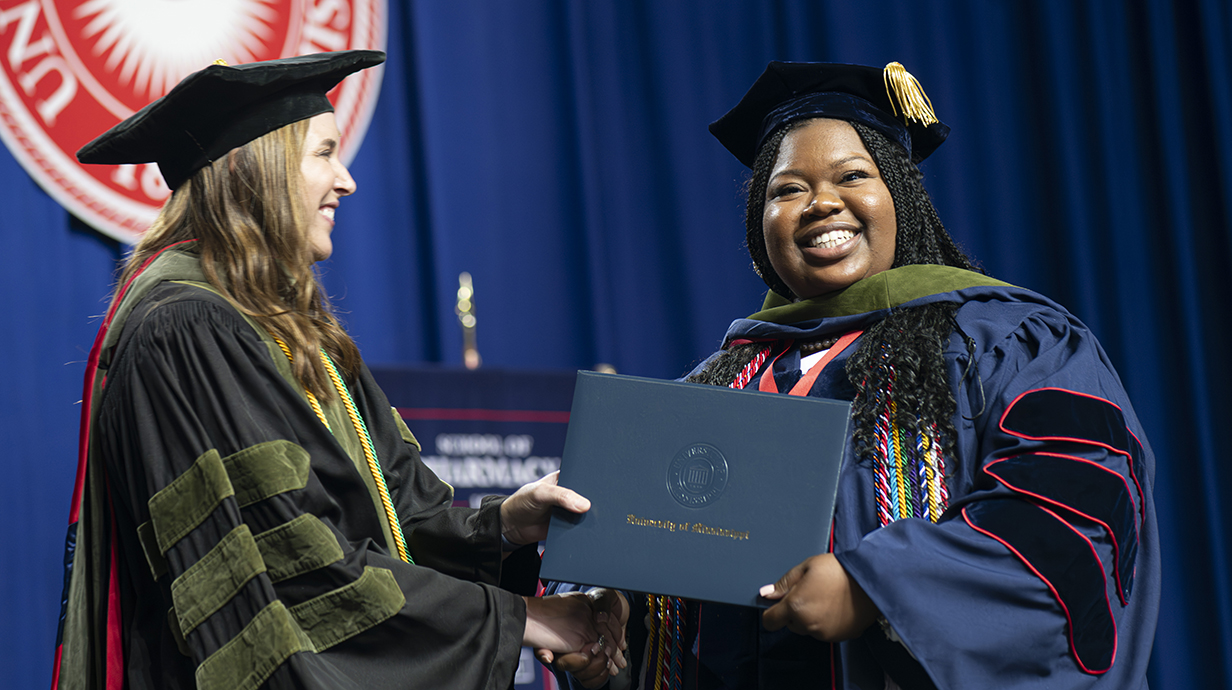 A student smiles as she accepts her diploma cover on stage during commencement