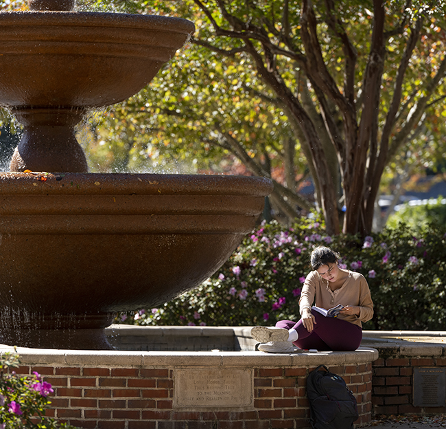 A student sits on the edge of the Phi Mu fountain and studies a book in between classes.