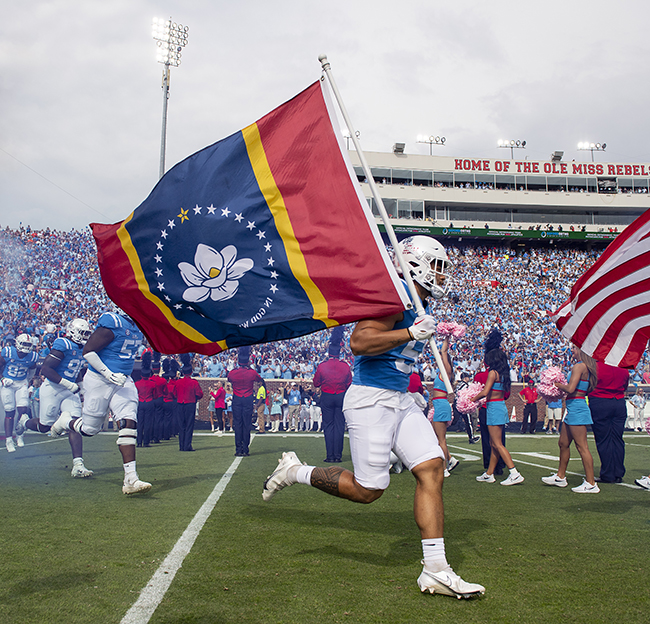 A football player runs across the field during a home game with the Mississippi state flag