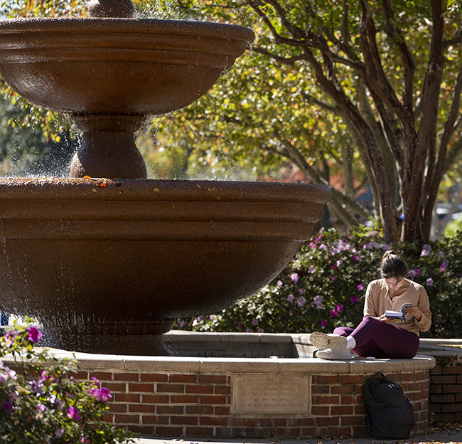 A student takes a moment to read a book at the Phi Mu Fountain in the Quad.