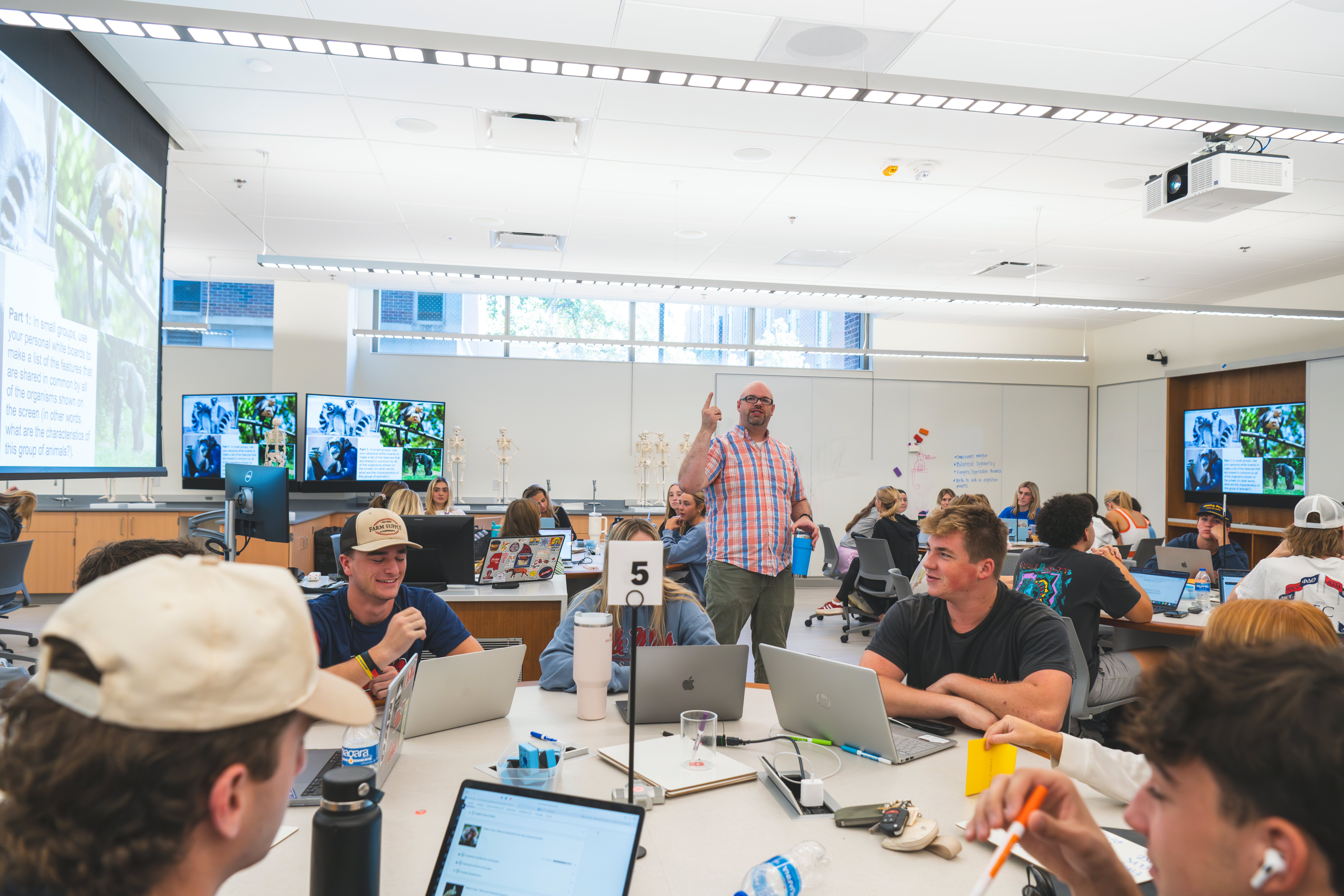 bio teal room in which student listen in class at their tables and their teacher is explaining something to them 