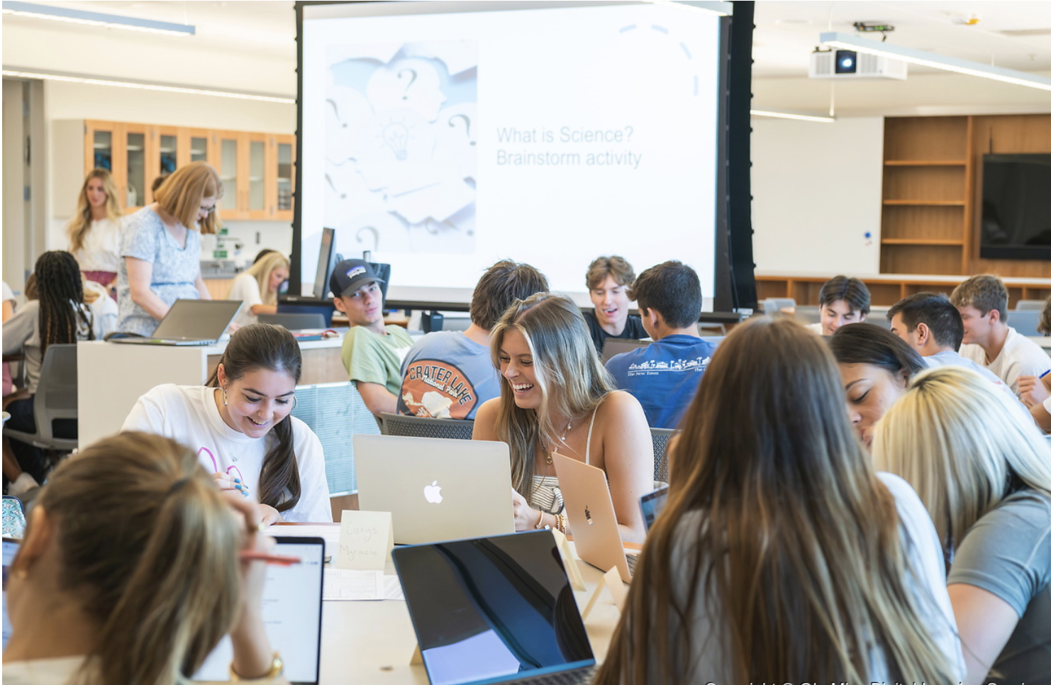 students in a teal room at round tables in class sitting