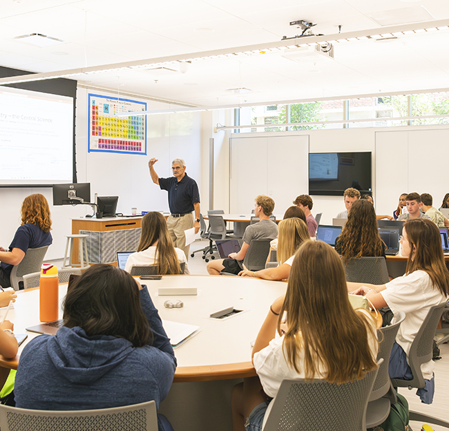 Professor teaches a STEM class while students work at tables in a modern classroom.