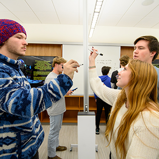 3 people drawing at a white board from both sides