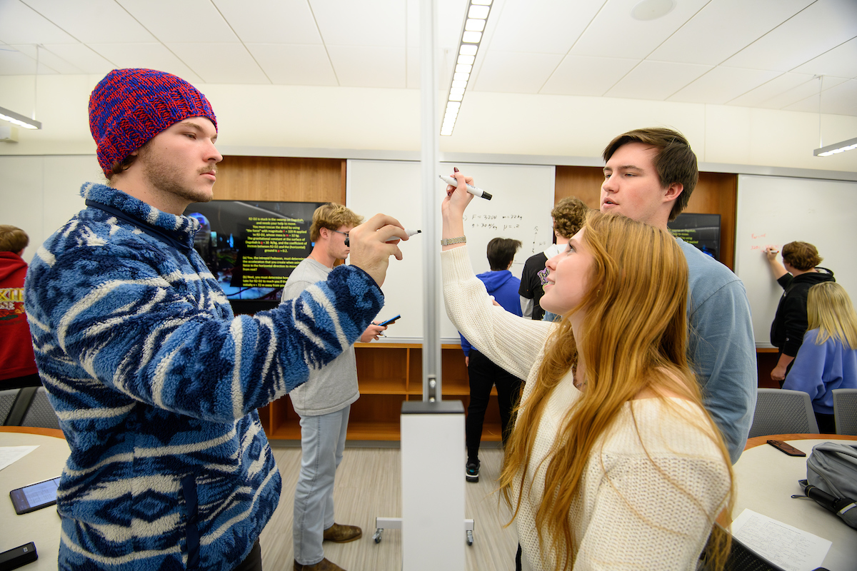 Students writing on both sides of a white board 