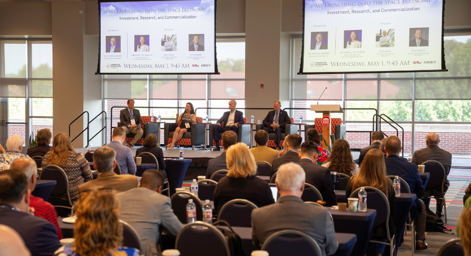 Four people speak in front of an audience during a panel discussion.