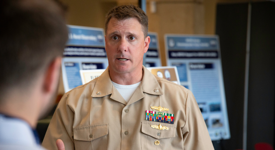 A man in a military uniform speaks to another person.