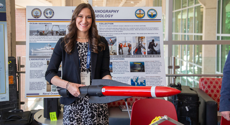 A woman holds a model rocket in front of a research poster.