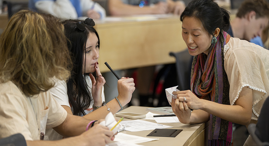 A woman helps two students complete an assignment in a tiered classroom.