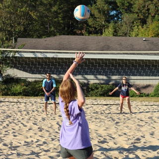 three students playing sand volleyball