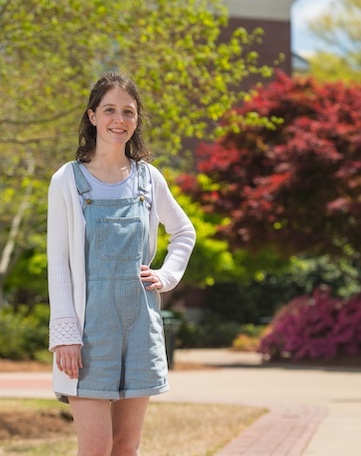 student standing outside on campus surrounded by flowering trees and shrubs