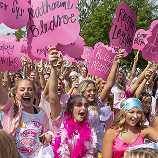 Current Phi Mu members hold up signs and await new members to run down Sorority Row on Bid Day