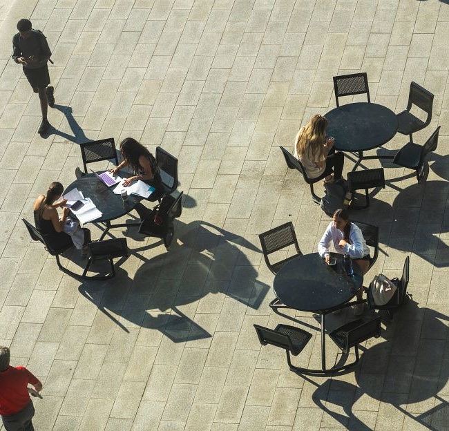 Students study at tables outdoors as others walk by. 