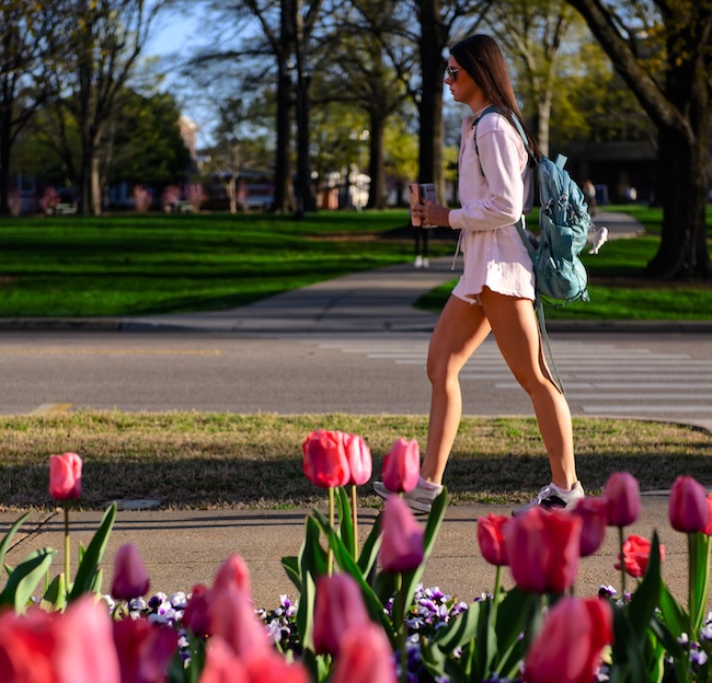 A student walks past flowers on campus.