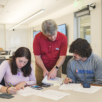 A faculty member assists two students during class and points at one of their notes