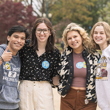 Four students stand together and smile in the grove. The student on the far left holds up a thumbs up. 