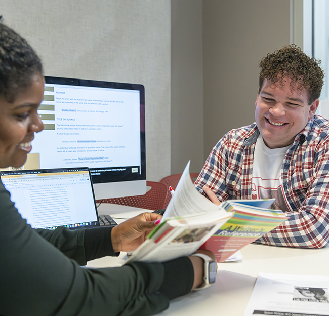 A student smiles as he is assisted by a Writing Center staff member