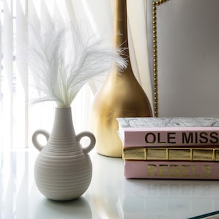 stack of book stating "Ole Miss" next to a ceramic pot and lamp