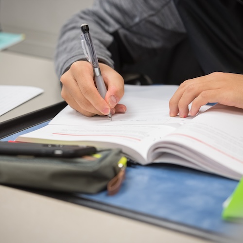 Student writing with a mechanical pencil and textbook